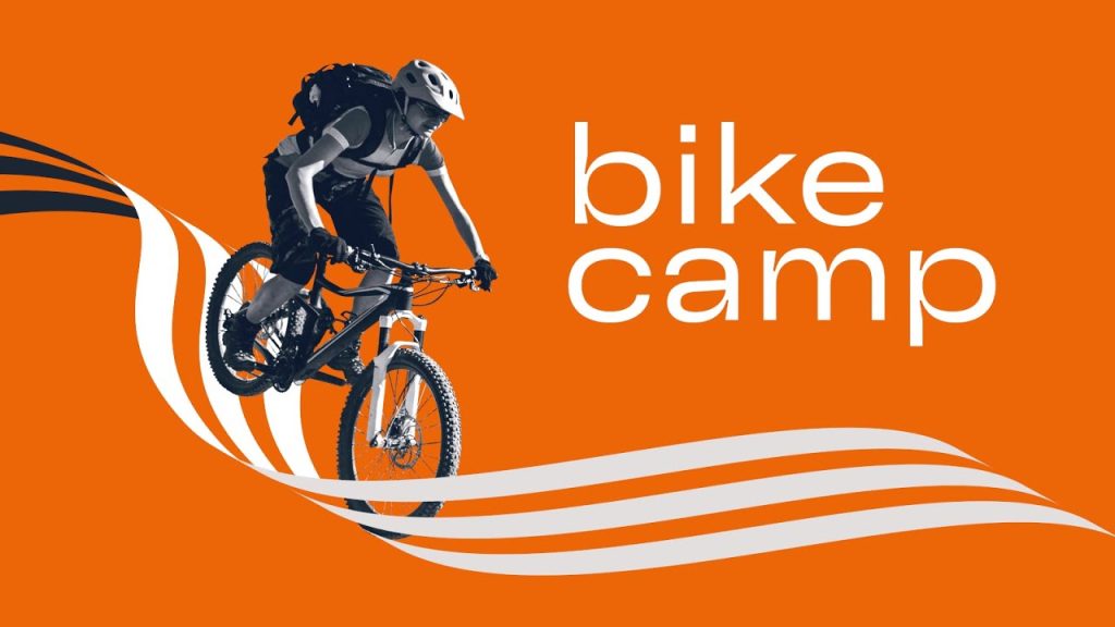 Ein Radfahrer auf einem Mountainbike, mit dem Text "Bike Camp" in Fettdruck vor einem leuchtend orangefarbenen Hintergrund.